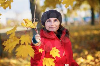 Woman in a beret and red jacket on the background of golden autumn maple leaves. Shallow depth of field. Selective focus on model.