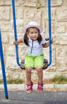 Baby girl on a swing. Child in a white hat to play outdoors.