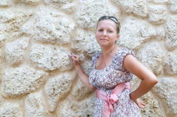 Cute young woman in sundress standing leaning on vintage wall of limestone. Selective focus on model.