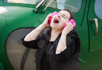 Woman enjoying music with pink fur headphones on the background of the green helicopter cabin. She enjoys music.