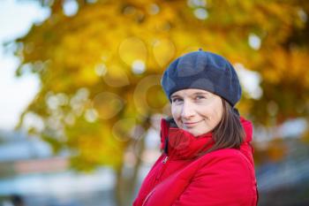 Portrait of a smiling young woman in a beret on the background of golden autumn leaves. Shallow depth of field. Selective focus on model.
