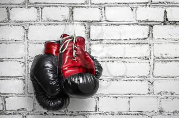 A pair of old boxing gloves hanging against a white brick wall.