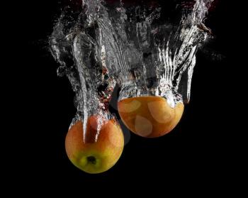 Apples are falling into the water with a splash on a black background.