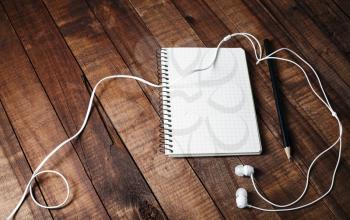 Photo of blank notebook, pencil and headphones on vintage wooden table background. Template for design portfolios.