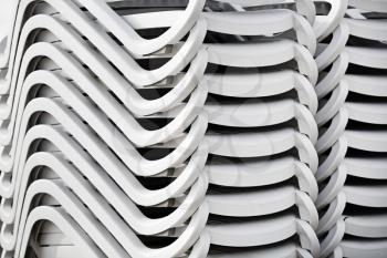 Folded stack of white plastic deck chairs. Pile of beach loungers. Abstract background or texture