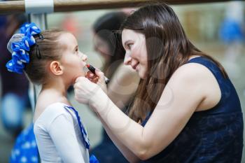 Mother makes make-up her daughter. Mother putting lipstick on her daughter on mirror background. Mom helping little daughter to use lipstick before a dance performance. Shallow depth of field. Selecti