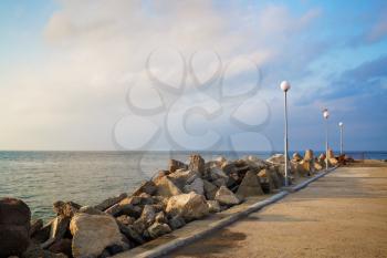Breakwater with lampposts. Pierce with boulders on the Black Sea coast. Summer day.