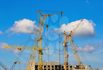 Yellow tower cranes and mobile construction cranes against blue sky background