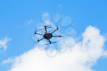 Flying hexacopter drone against a blue sky with clouds.