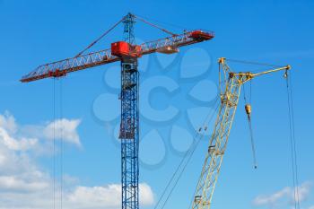 Two construction cranes. Tower crane and mobile construction crane against blue sky background.