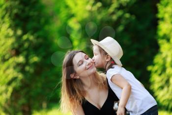 Child kisses his mother. Happy family against a background of lush green foliage. Selective focus. Space for text.