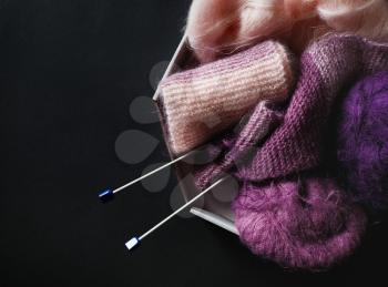Purple and pink yarn and knitting needles on black paper background. Flat lay.