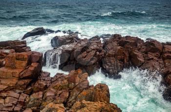 Stormy sea waves crash against a rocky shore. Waves crashing over rocks. Scenic seascape.