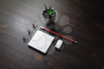 Stationery set on wood table background. Blank notes, pencil, eraser, and plant. Responsive design mockup.