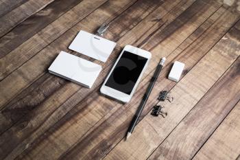 Smartphone with blank screen, business cards, badge, pencil, eraser and metal clamps on wood table. Blank stationery template.