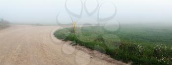 Gravel road turning in the fog. Morning in the countryside. Rural landscape. Panoramic shot.
