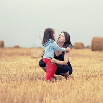Mother and her daughter child girl hugging in the field against straw bales background. Selective focus on the models. Toned image.