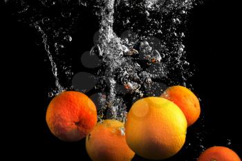 Clementines falling in water with splash on black background.