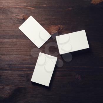 Three blank white business cards on dark wooden background. Mockup for branding identity. Flat lay.