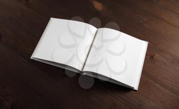 Photo of opened book with blank white pages on wooden background.