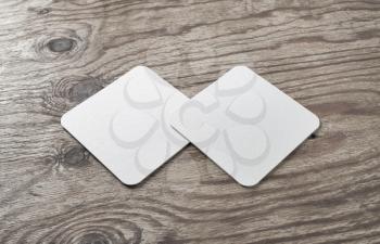 Blank white square beer coasters on wood table background.