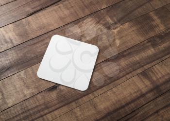 Blank square beer coaster on wooden background.