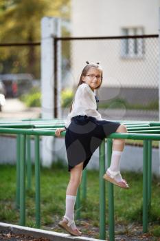 Child girl climbs on the horizontal bar. Schoolgirl at the playground. Vertical shot. Selective focus.