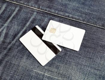 Photo of two blank credit cards on gray denim background. White bank cards. Mockup for branding identity. Copy space for placing your design.