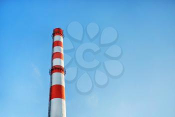 Factory chimney with red and white stripes against blue sky background.