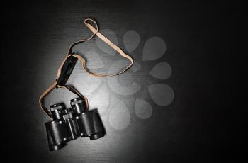 Photo of black binoculars on black wood table background. Lot of copy space for your text. Flat lay.