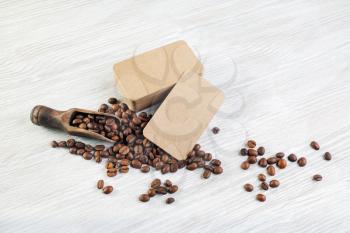 Roasted coffee beans and kraft paper business cards on light wood table background. Responsive design mockup.