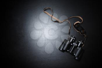 Photo of old black binoculars on black wooden background. Copy space for your text. Top view. Flat lay.