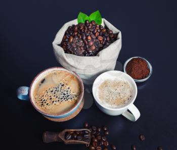 Hot coffee cups and coffee beans in canvas bag and ground powder on black kitchen table background.