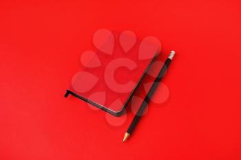 Black notepad and pencil on red paper background. Copy space for your text.