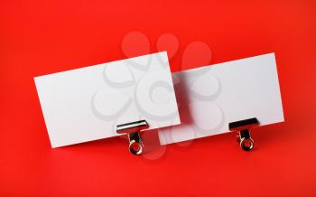 Photo of two blank business cards and metal binder clips on red paper background. Branding ID template.