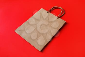 Brown paper bag with handles on red paper background.