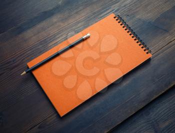 Blank orange sketchbook and pencil on wood table background. Responsive design template.
