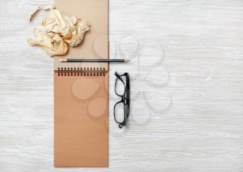 Opened notebook with blank craft paper pages, glasses, pencil and crumpled paper on light wood table background. Flat lay.