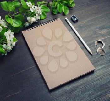 Branding stationery mockup. Kraft notebook, pencil, sharpener and spring flowers on wooden background. Blank objects for placing your design.