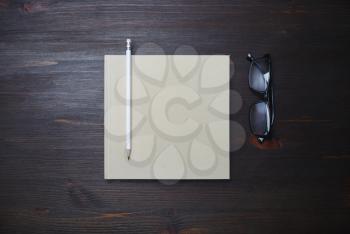 Blank closed book, pencil and glasses on wood table background. Stationery template. Flat lay.