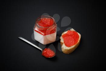 Delicious fresh red caviar. Sandwich with red caviar, glass jar and spoon.