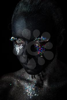 Conceptual art Portrait of Beautiful Woman in Black makeup with Sparkles on a Face isolated on a dark background