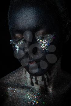 Conceptual art Portrait of Beautiful Woman in Black makeup with Sparkles on a Face isolated on a dark background