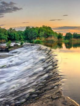 Beautiful view of the dam on the Southern Bug River at sunset. Village of Migiya, Ukraine, on a sunny summer evening