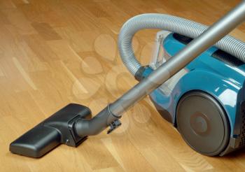 Blue vacuum cleaner with black wheels on a oak parquet