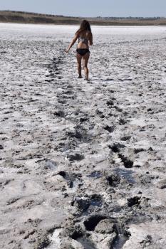 Woman walking along the dry bottom of a salt lake, rear view. Walk the dark-haired woman in a swimsuit on the bottom of a dry lake with salt and mud. The ancient dried-up lake.