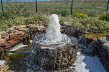 Small fountain in the flower bed area. Water jet climb up.