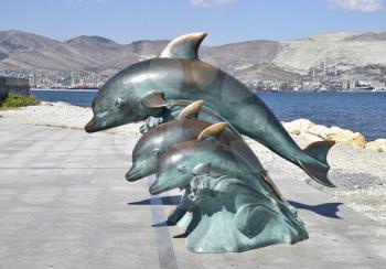 The bronze sculpture of three dolphins on the beach.