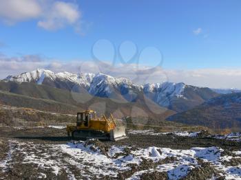 Crawler tractor with grederom against the backdrop of snow-capped mountains. Alignment grederom area for technological needs.