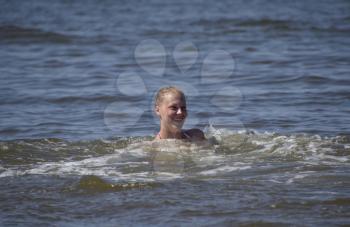 Blonde girl laughs and enjoys swimming in the sea water. Girl on a background of sea water immersed in water up to their necks. Beautiful young woman.